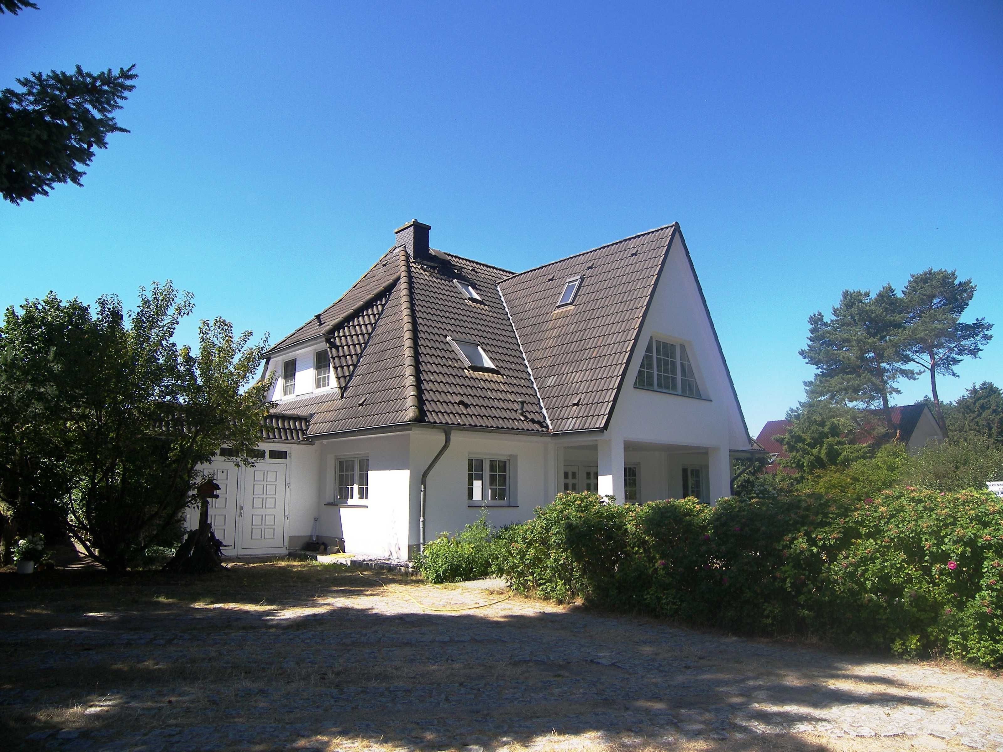Une maison à deux étages, avec un toit en pente, des murs extérieurs blancs et un porche à l’avant.