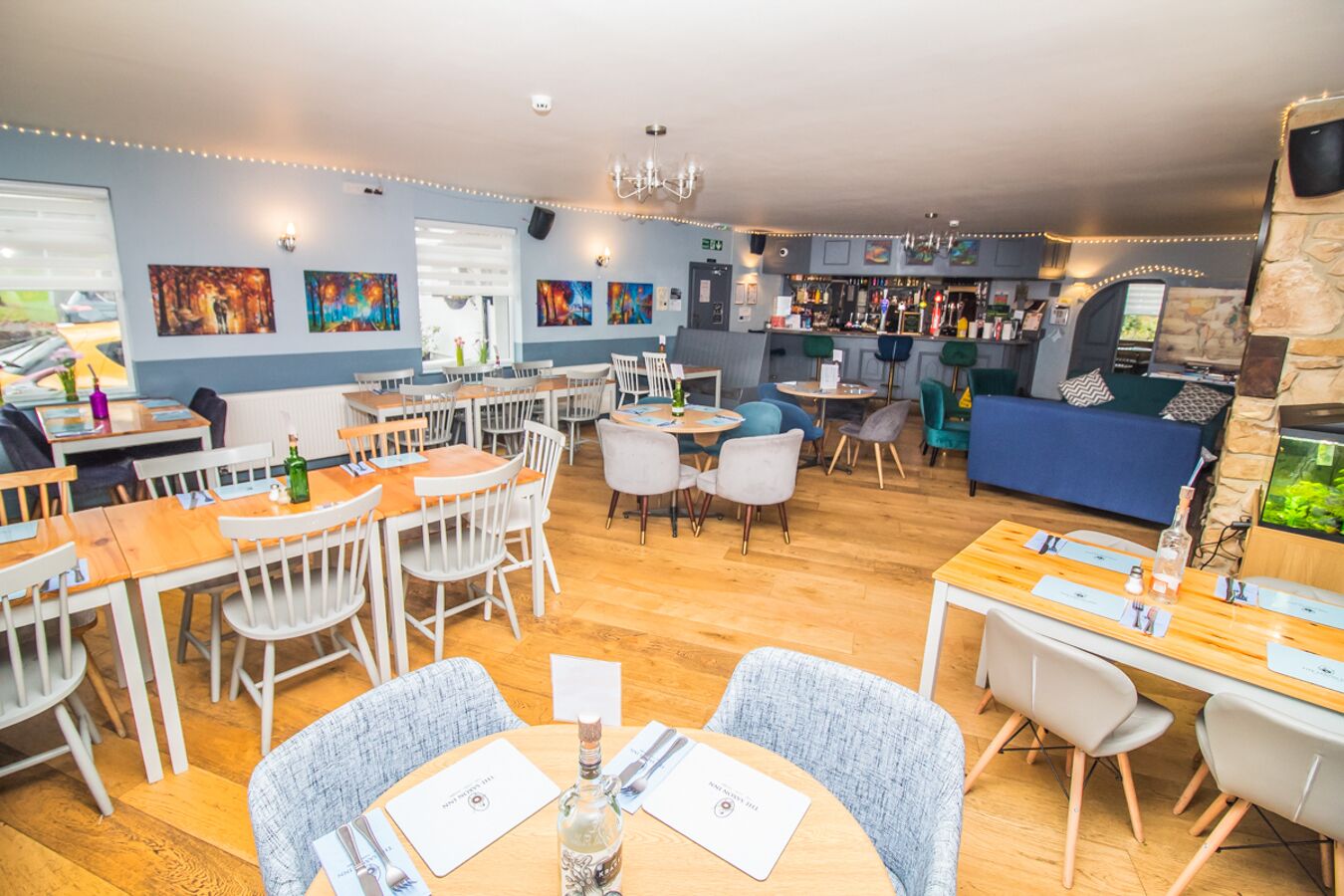 A restaurant with wooden tables and chairs, a bar area, and artwork on the walls.