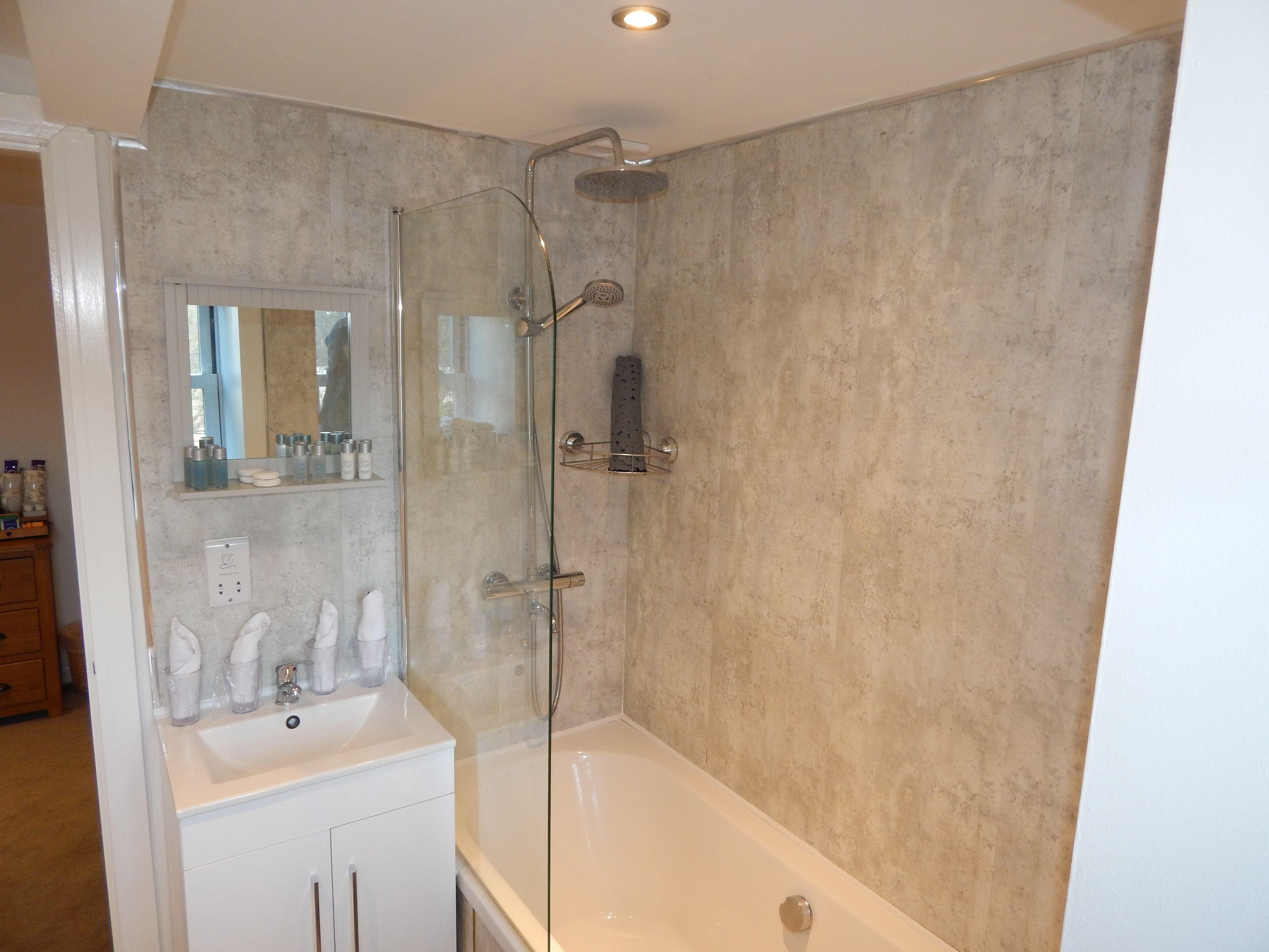 Un baño moderno con ducha de vidrio, un lavabo blanco y un espejo encima.
