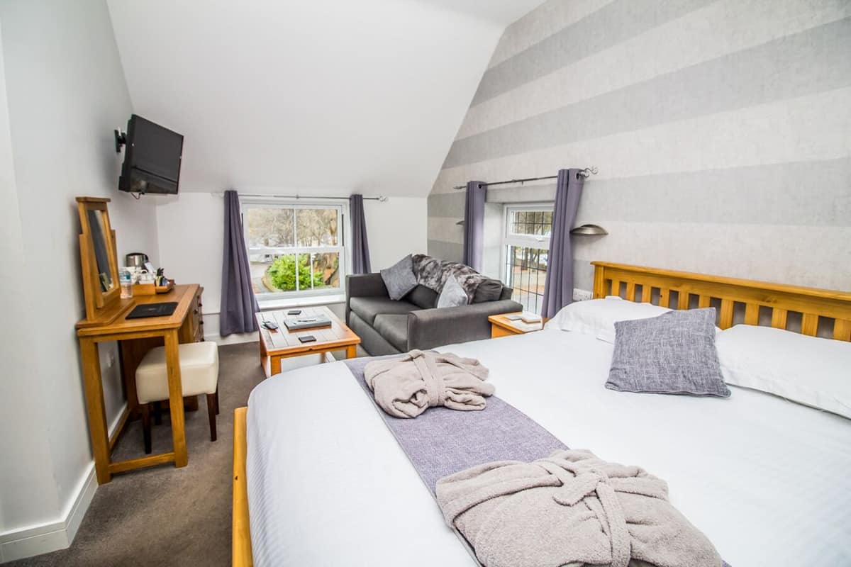 Ein Schlafzimmer mit einem Bett, einem Schreibtisch, einem Sessel, einem Fernseher und einem Fenster mit Vorhängen.