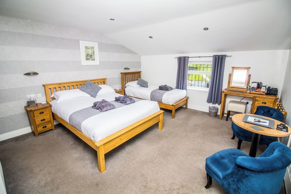 Ein Hotelzimmer mit zwei hölzernen Betten, einem Schreibtisch mit Stuhl, einem kleinen Tisch und einem Fenster mit Vorhängen.