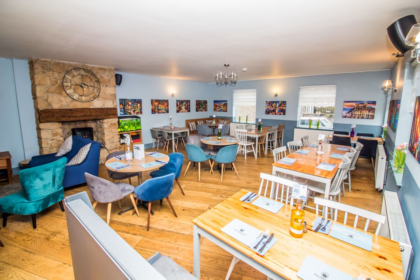 Un restaurant avec des tables et des chaises en bois, une cheminée en pierre et des œuvres d’art accrochées aux murs.