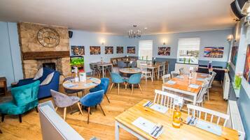 Un restaurant avec des tables et des chaises en bois, une cheminée en pierre et des œuvres d’art accrochées aux murs.