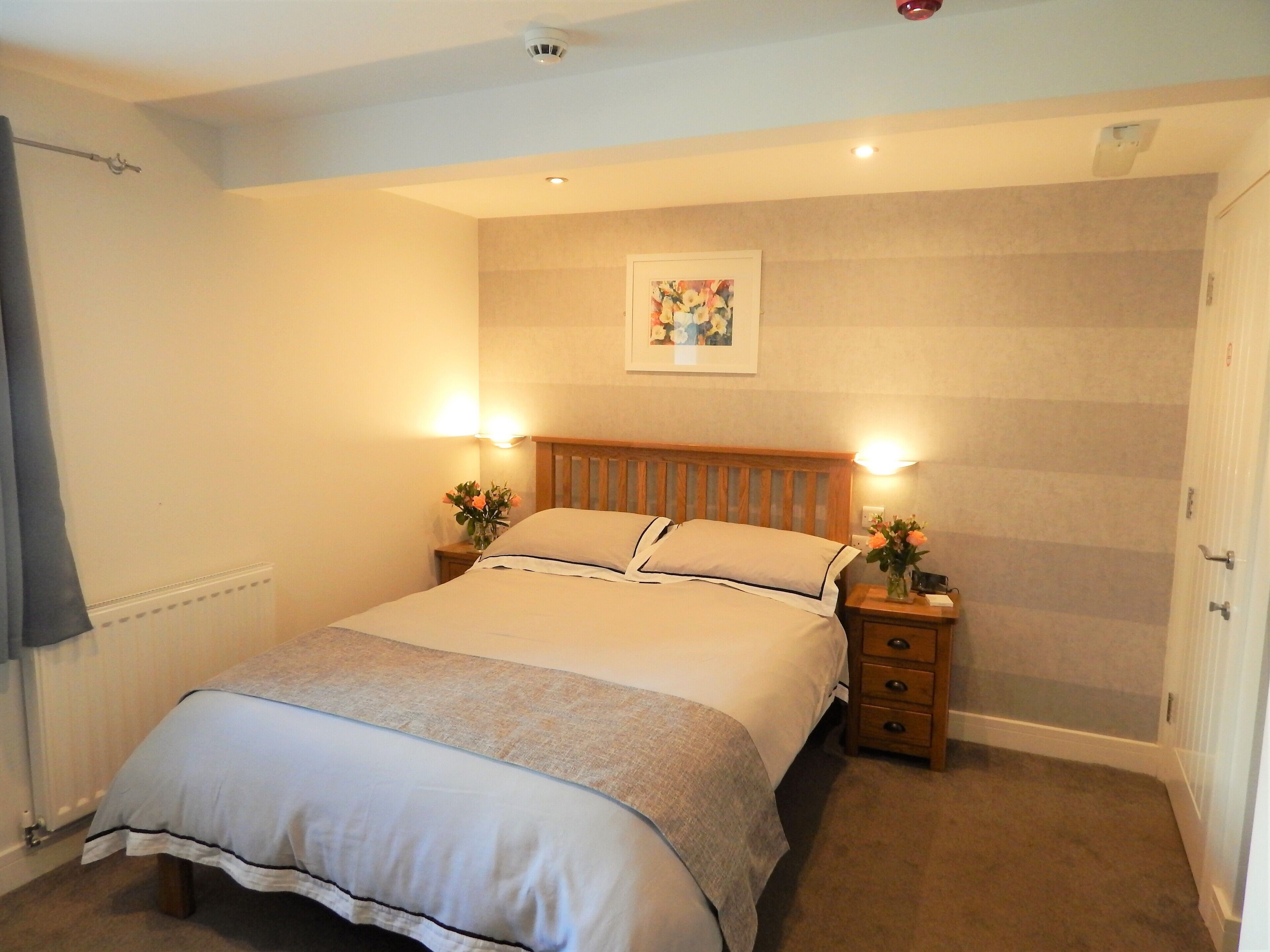 A neatly made bed with a wooden headboard, two bedside tables with lamps, and a framed picture on the wall.