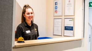 A hotel reception desk with a name tag, a yellow bell, and framed awards on the wall. - The Saxon Inn (Bishop Auckland)