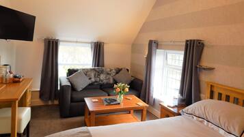 Una habitación acogedora con cama, sofá, una mesita, televisor y ventana con cortinas.