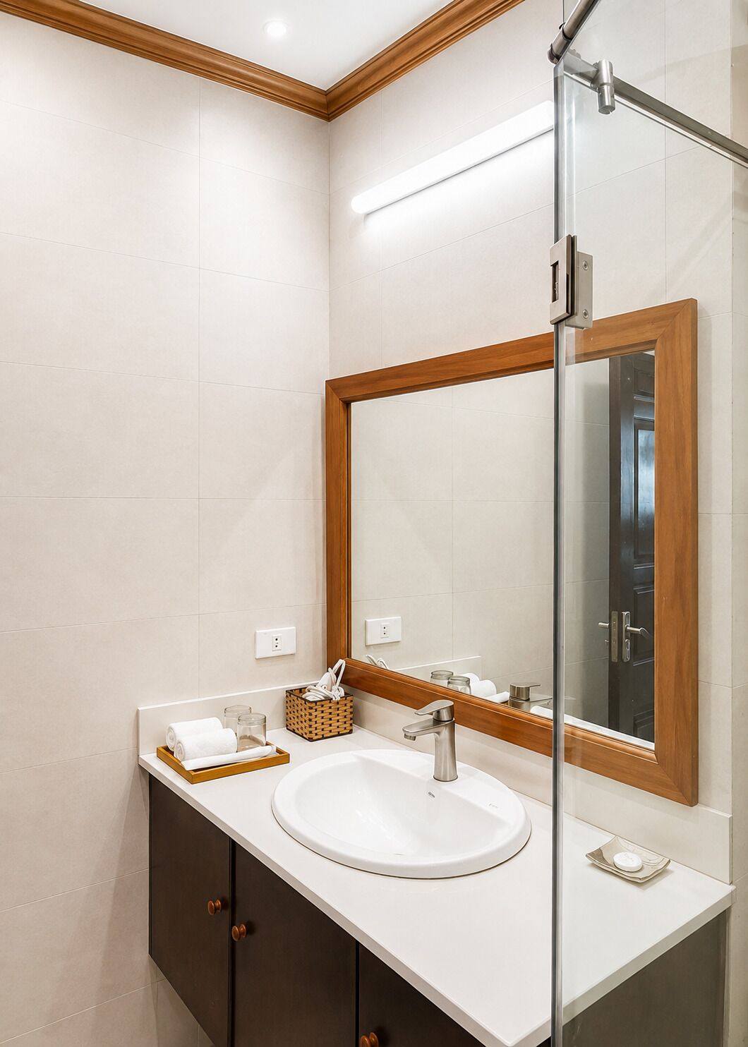 A modern bathroom with a white sink, dark cabinets, a wooden-framed mirror, and a glass shower enclosure.