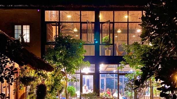 A building with multiple floors, large windows, and outdoor seating areas with tables and chairs.