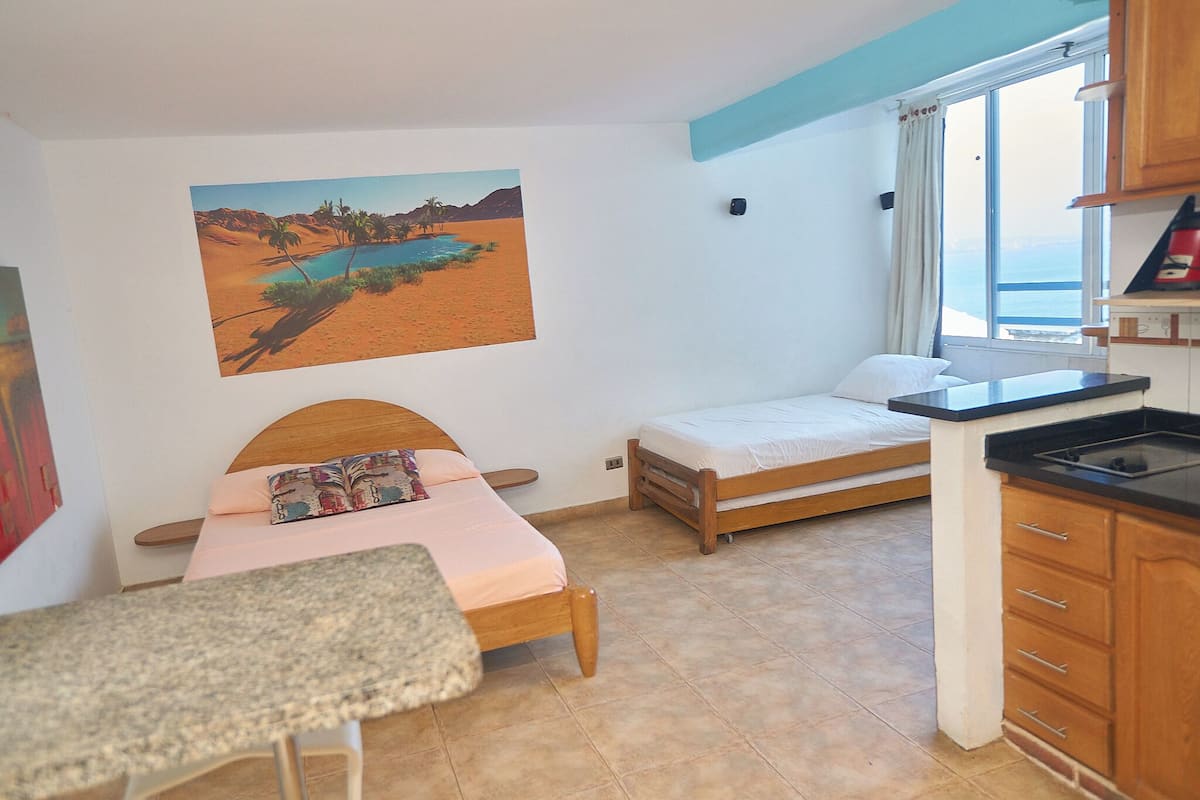 Une chambre à coucher avec un lit, un petit bureau, une fenêtre avec des rideaux et un tableau accroché au mur.