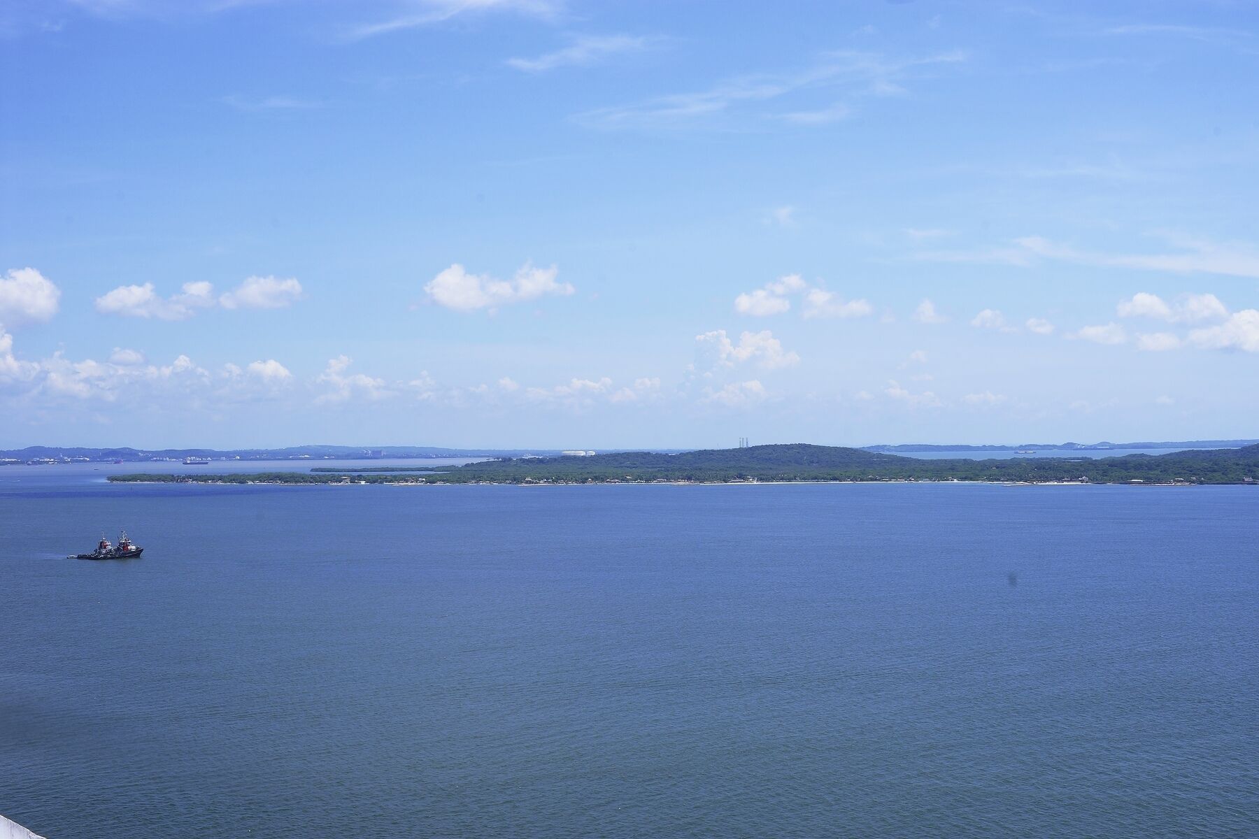 A calm sea with a small boat in the distance and a distant shoreline with buildings.