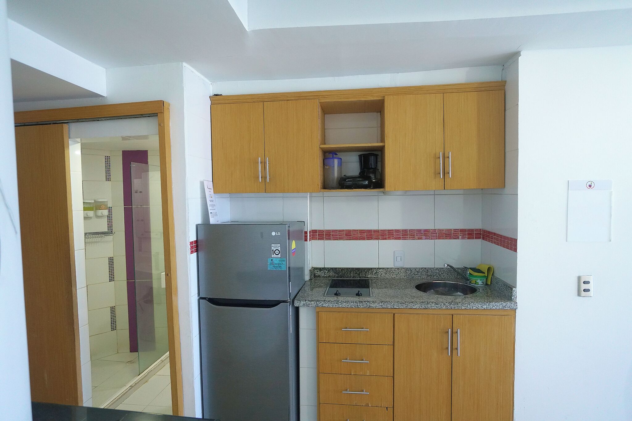 A compact kitchen with wooden cabinets, a stainless steel refrigerator, and a granite countertop.