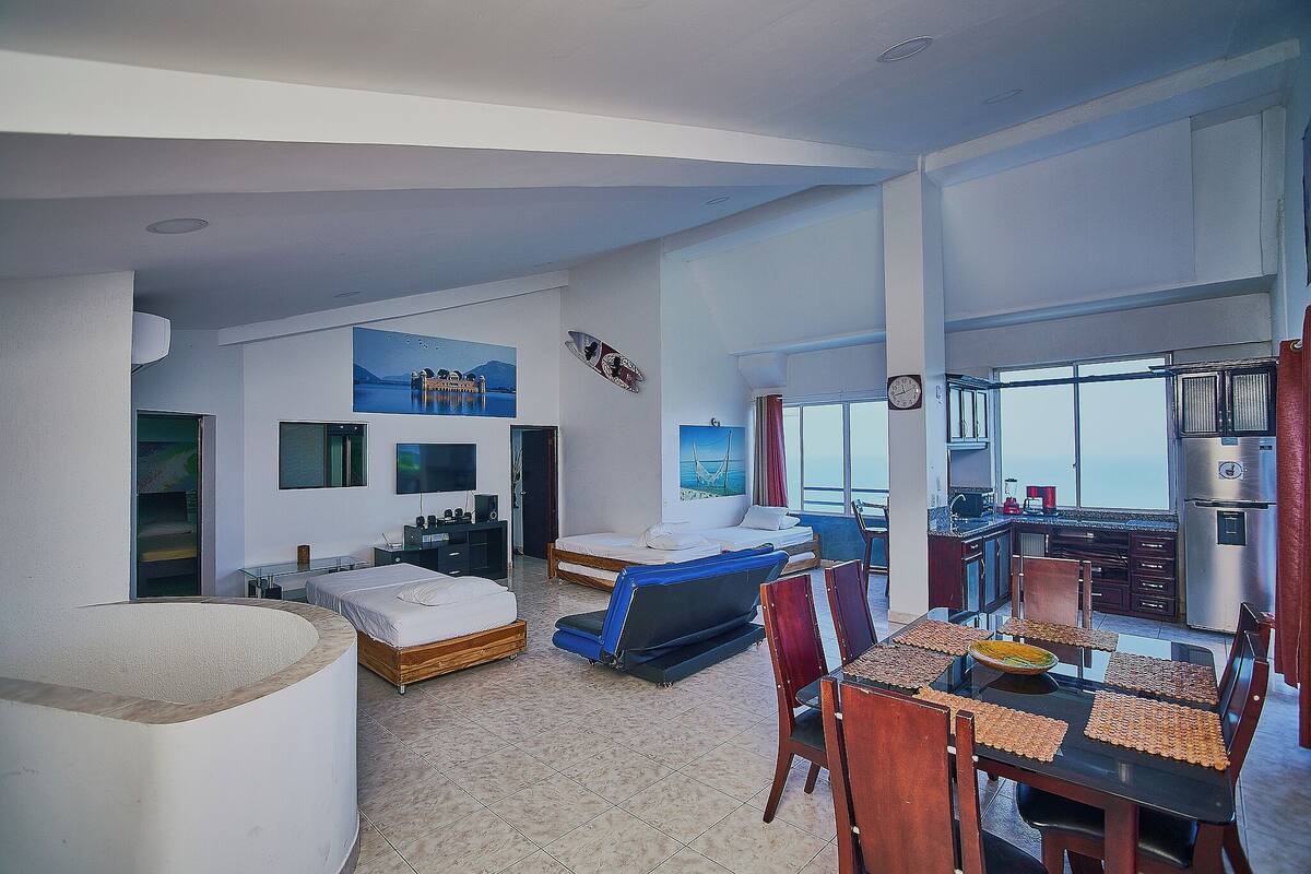 Une chambre d’hôtel moderne dotée d’un grand lit, d’un coin salon avec une table et des chaises, d’une baignoire et offrant une vue sur la mer.