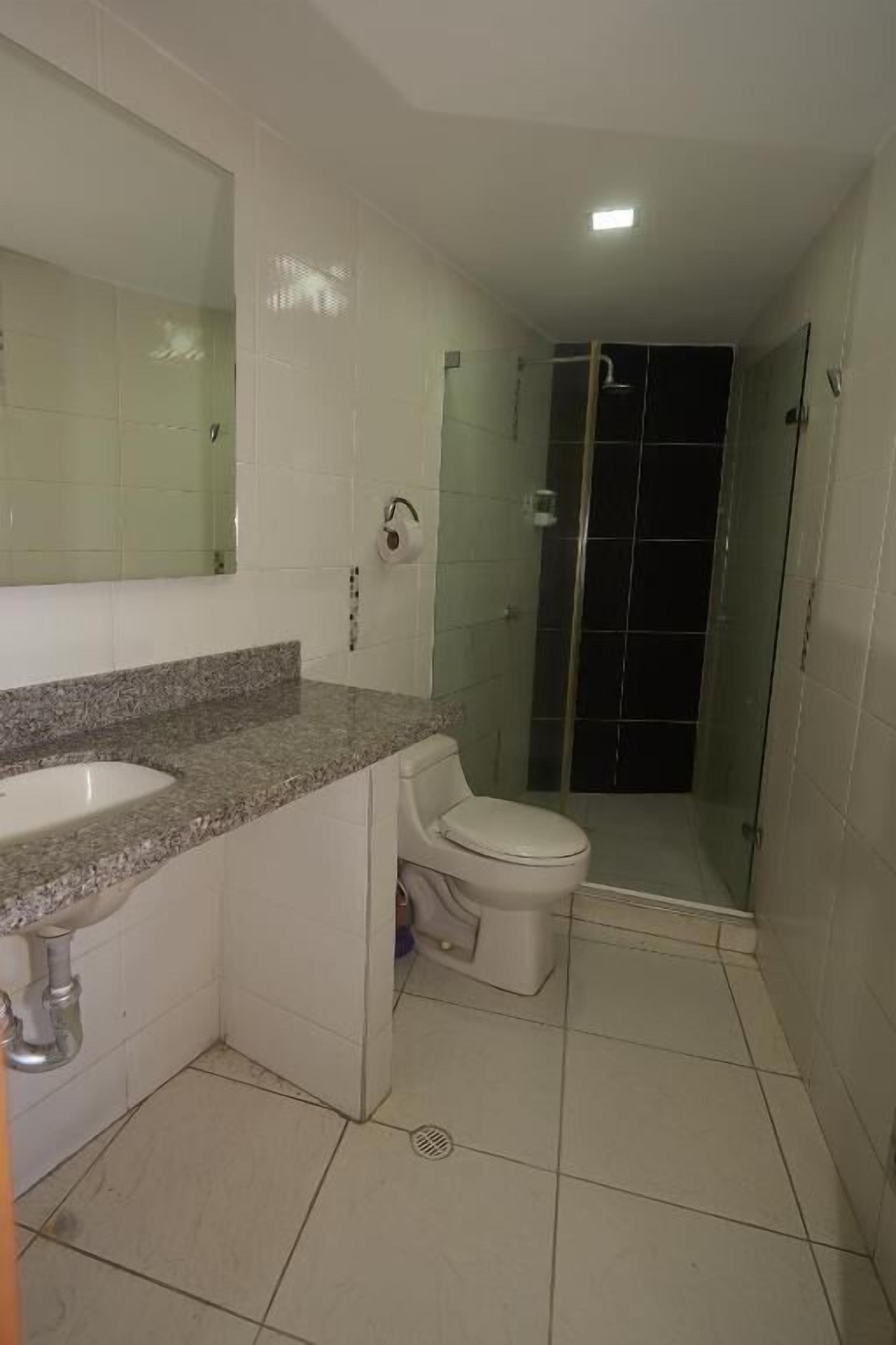 Une salle de bain avec un lavabo sur un plan de travail en granit, des toilettes et une cabine de douche en verre.