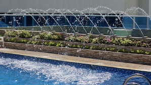 A swimming pool with water jets, a tiled deck, and a planter with flowers. - Apartamentos Bacanos (Cartagena)