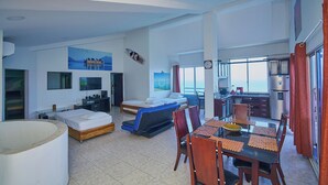 A modern hotel room with a bed, a sofa bed, a dining table with chairs, a kitchen area, and a large window with a view. - Apartamentos Bacanos (Cartagena)