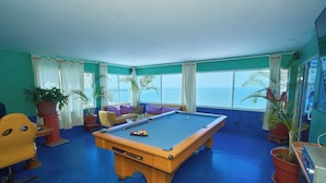 A pool table in a room with a view of the ocean, a sofa, and potted plants. - Apartamentos Bacanos (Cartagena)
