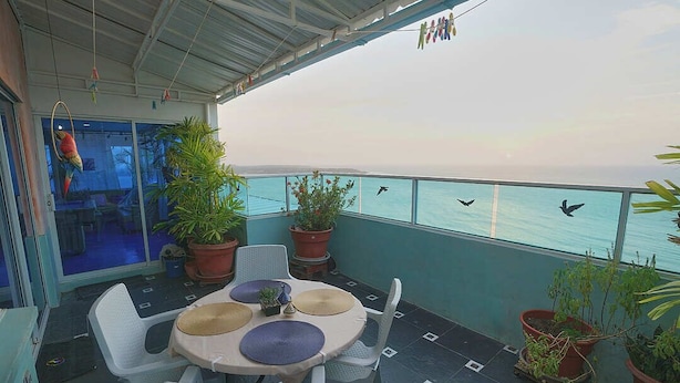 A balcony with a table and chairs, potted plants, and a view of the sea. - Apartamentos Bacanos (Cartagena)