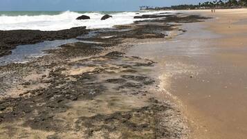 Uma praia com costa rochosa e ondas quebrando na areia.