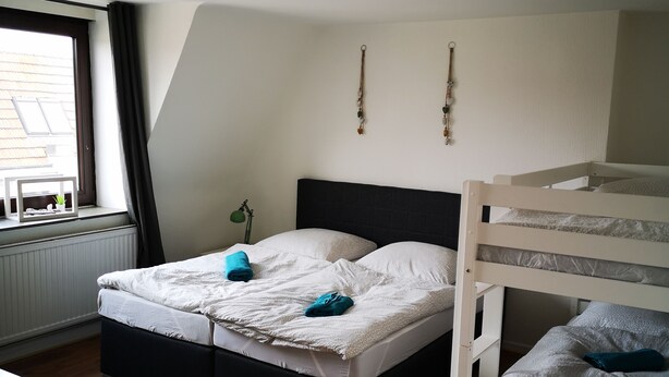Una habitación con literas, una cama individual, una mesita y una ventana con cortinas.