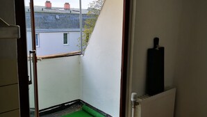 Una habitación con techo inclinado, un radiador y una ventana que ofrece vistas a edificios vecinos.