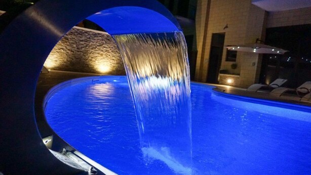 Una piscina con un elemento acuático circular y una pared de piedra al fondo.