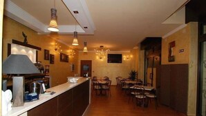 Un vestíbulo de hotel con mostrador de recepción, varias mesas de comedor y lámparas colgantes.