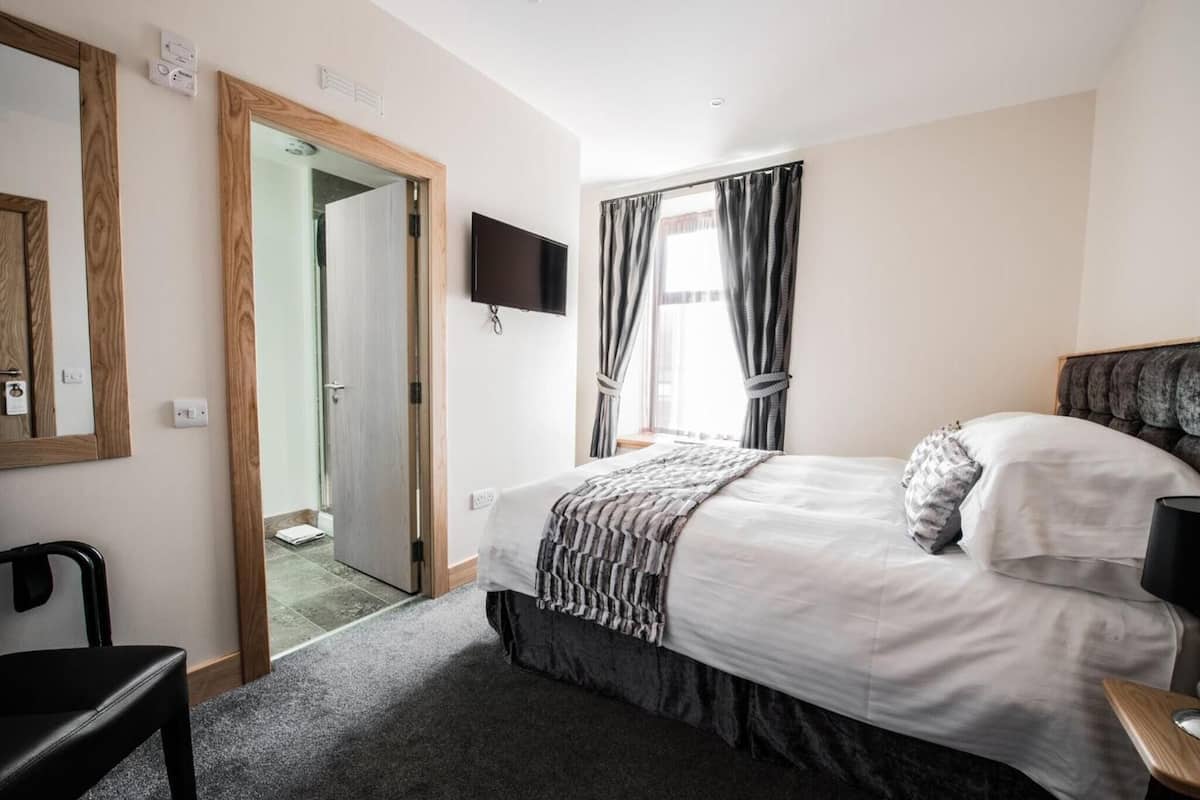 A hotel room with a bed, a TV mounted on the wall, a chair, and a door leading to another room.