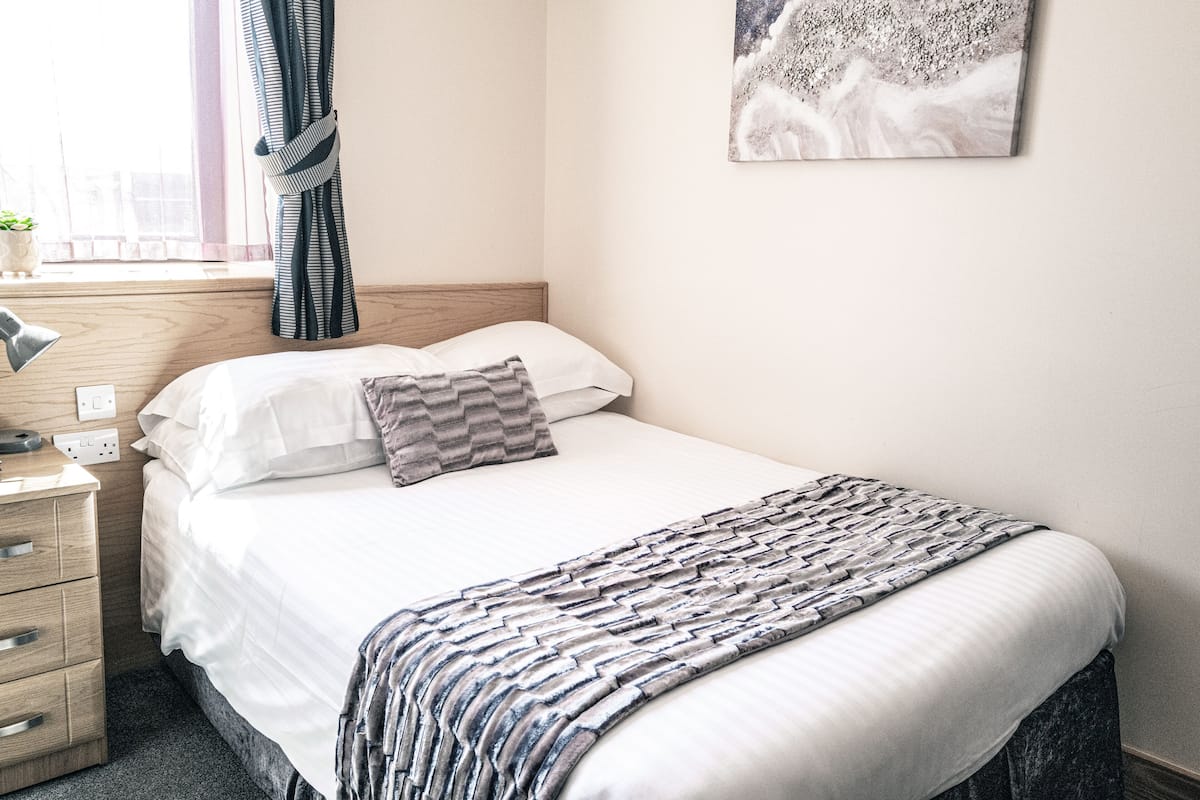 A neatly made bed with a striped blanket, a bedside lamp, and a pillow on a wooden nightstand.