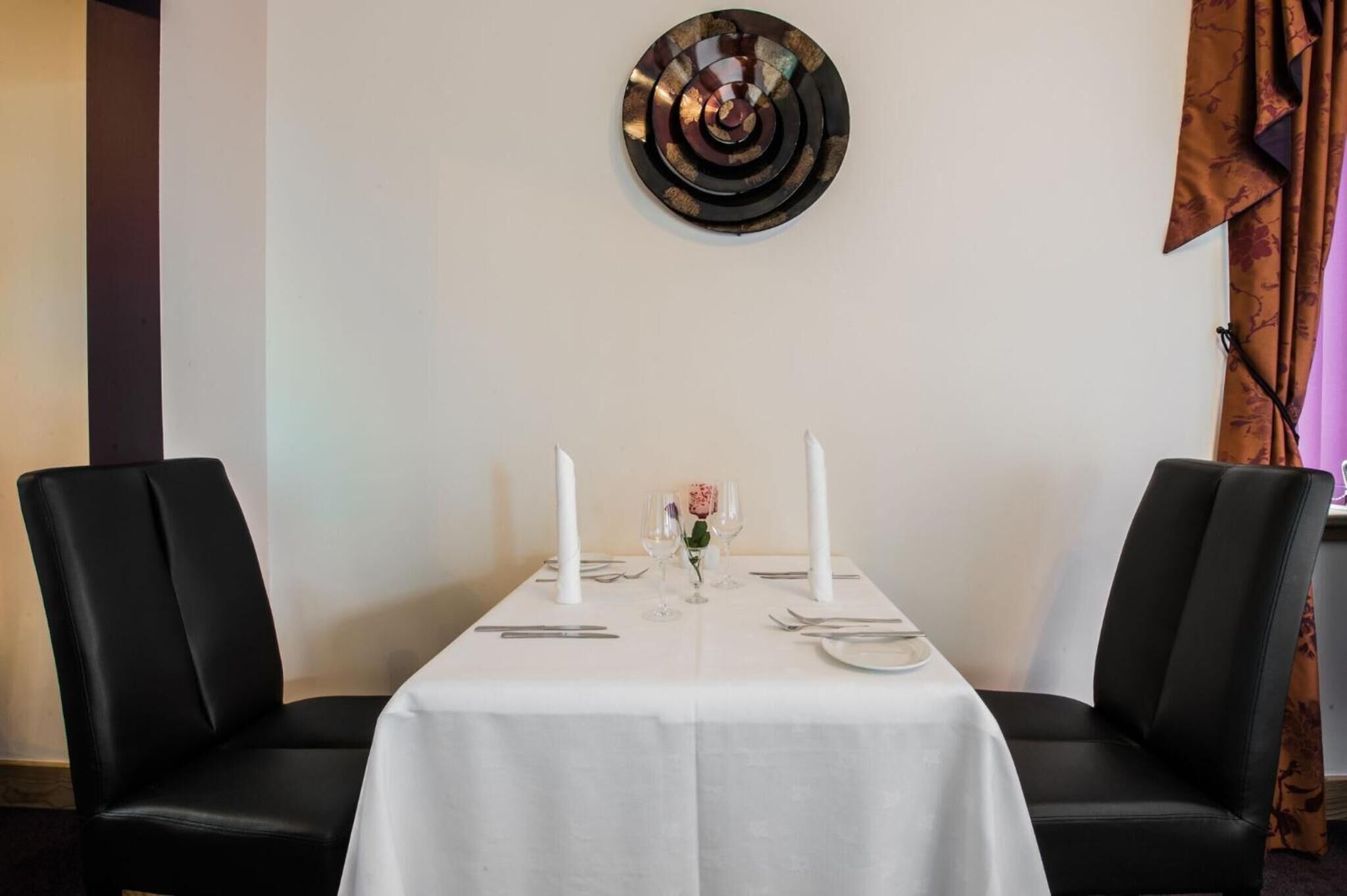 Una mesa para comer con mantel blanco, dos velas y un pequeño florero con una flor.