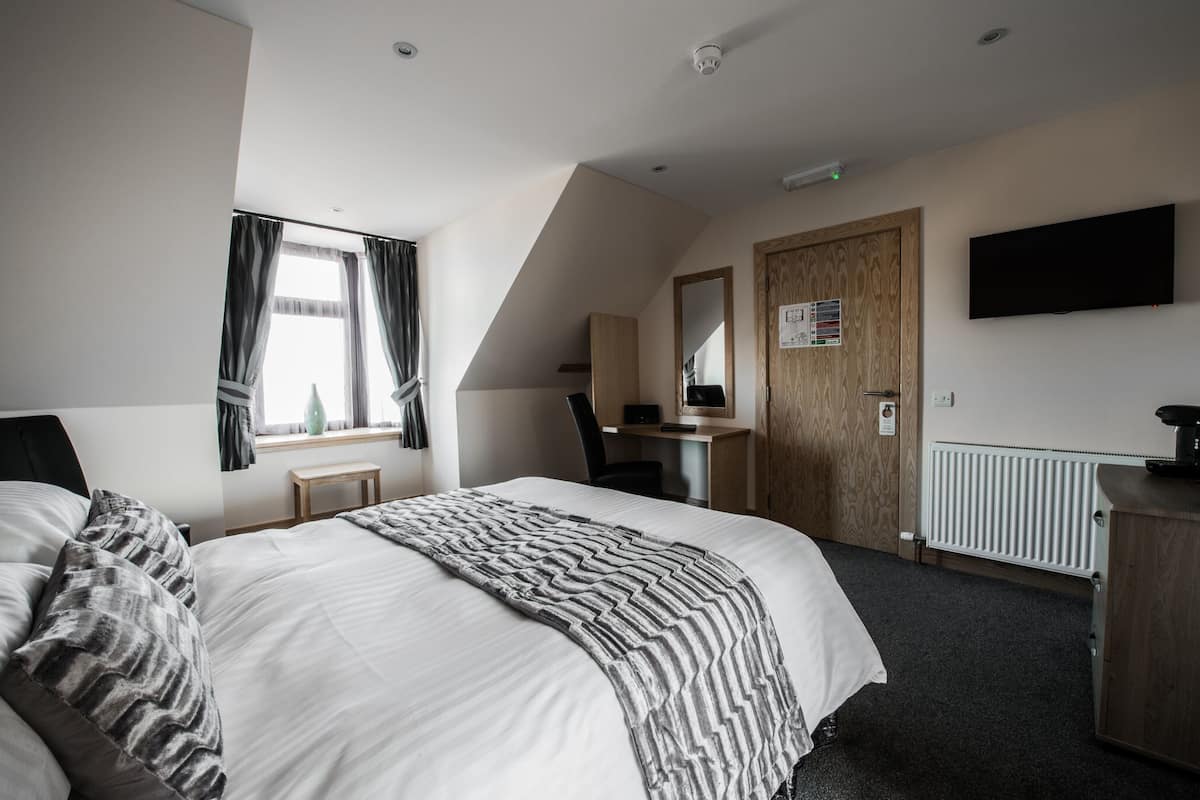 A hotel room with a large bed, a desk, a chair, a TV, and a window with curtains.