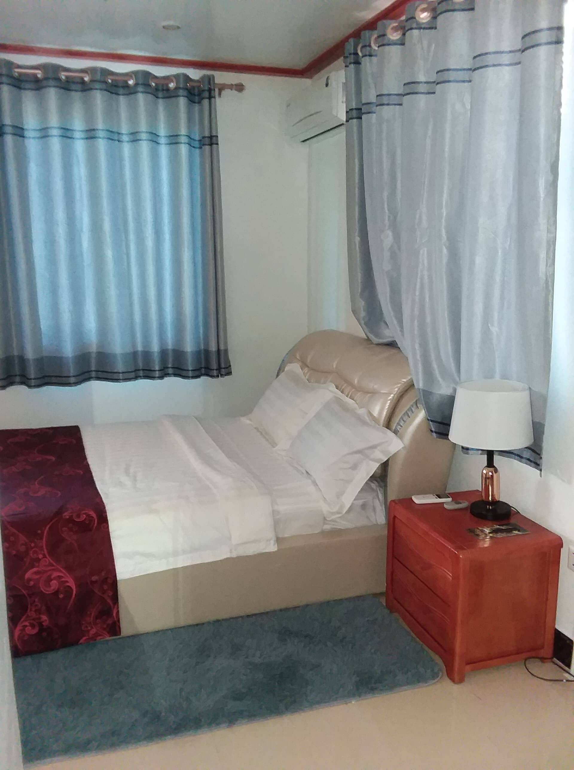 A bedroom with a bed, a bedside table with a lamp, and curtains.