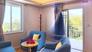 A room with a blue sofa set, a wooden table with a flower arrangement, and a view of greenery through the windows. - Riverside Hotel (Portsmouth)