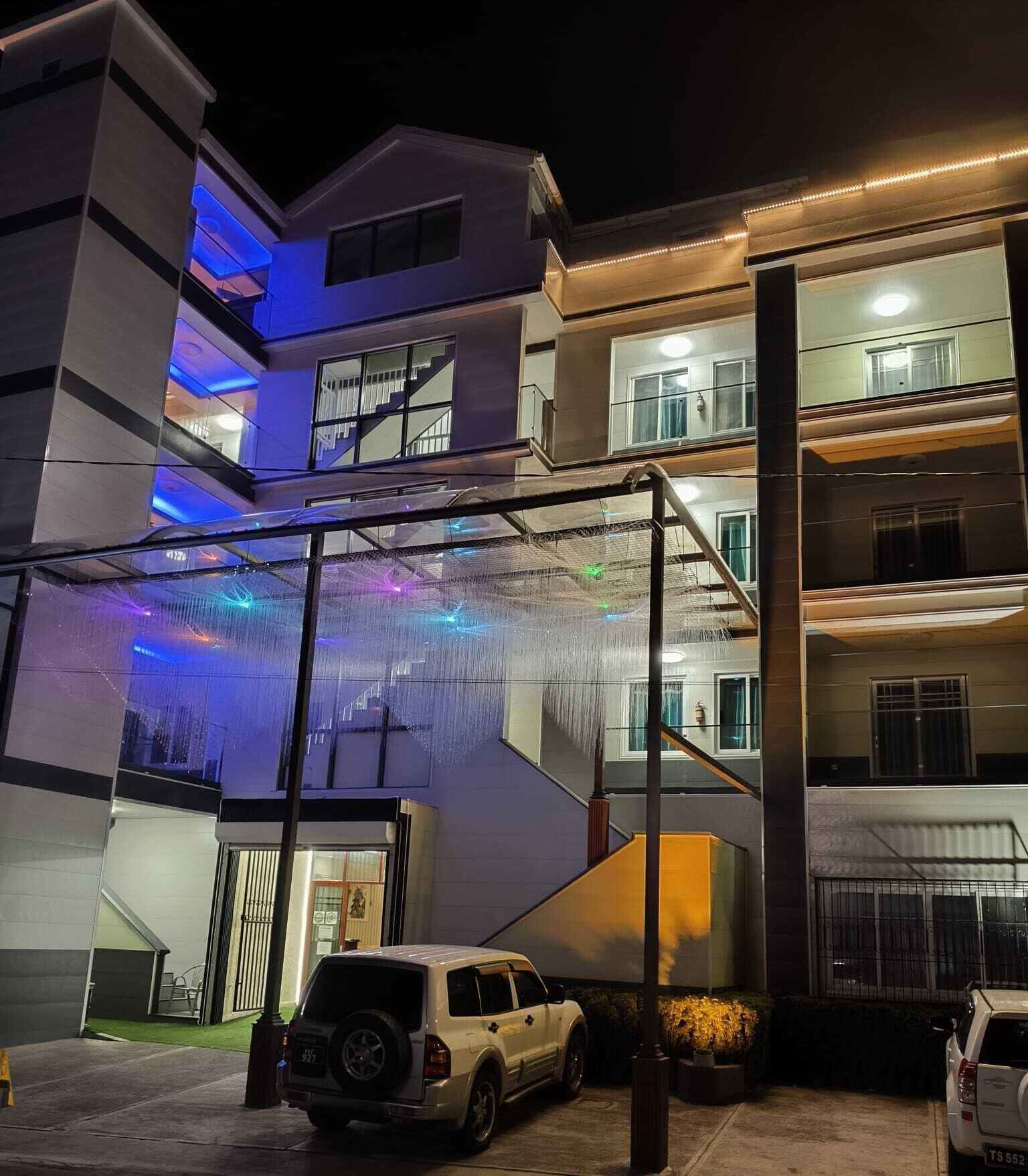 Un edificio de varios pisos con un espacio exterior techado, una escalera y coches estacionados.