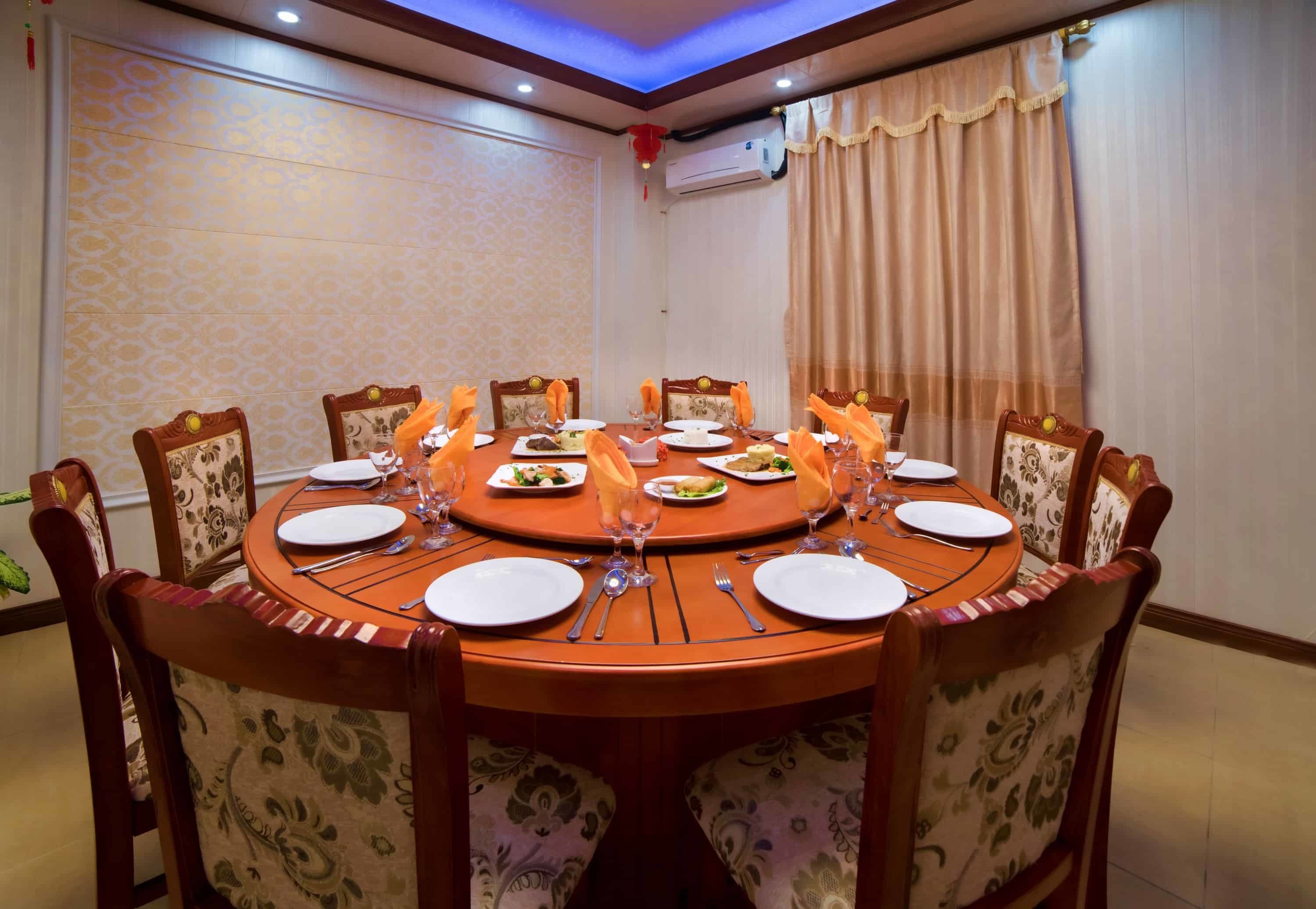 A round dining table with eight chairs, each with a floral-patterned cushion. The table is set with plates, cutlery, and glasses.