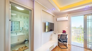 A modern bathroom with a glass shower enclosure, a white vanity, and a mounted TV. - Riverside Hotel (Portsmouth)