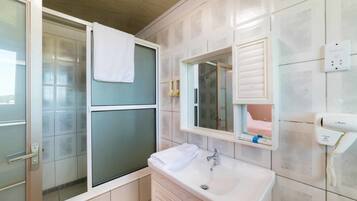 Un baño con cabina de ducha de vidrio, un lavabo blanco, un espejo y un secador de pelo en la pared.