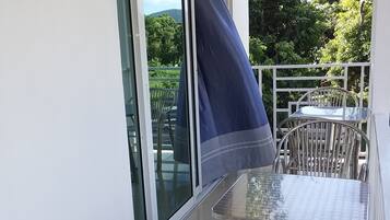 Un balcón con puerta de cristal, sillas de metal, una mesa de cristal y una toalla azul colgada en la puerta.