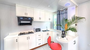 A modern kitchen with white cabinets, a microwave, a sink, and a red chair. - Riverside Hotel (Portsmouth)