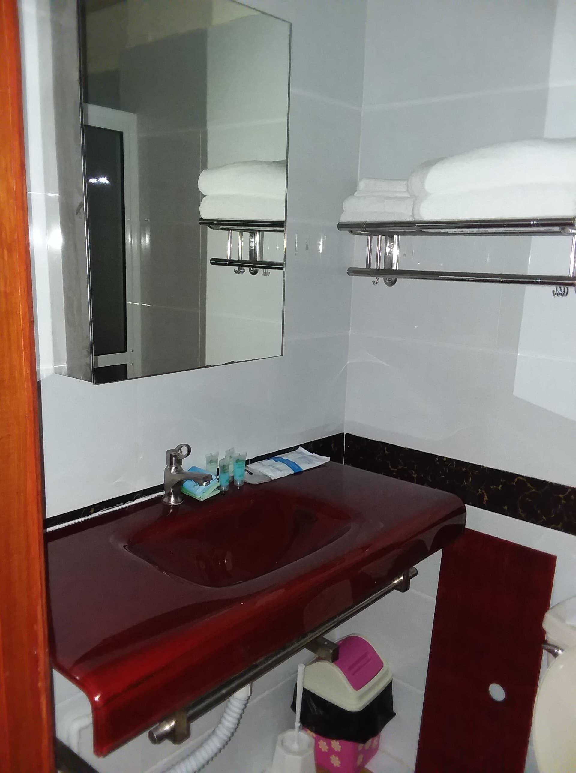 Casa de banho com uma pia vermelha, um espelho e duas barras de toalhas.