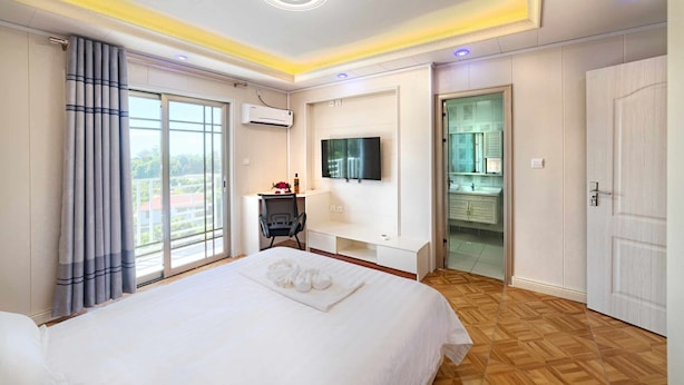A hotel room with a large bed, a desk with a chair, a TV mounted on the wall, and a bathroom visible through an open door. - Riverside Hotel (Portsmouth)