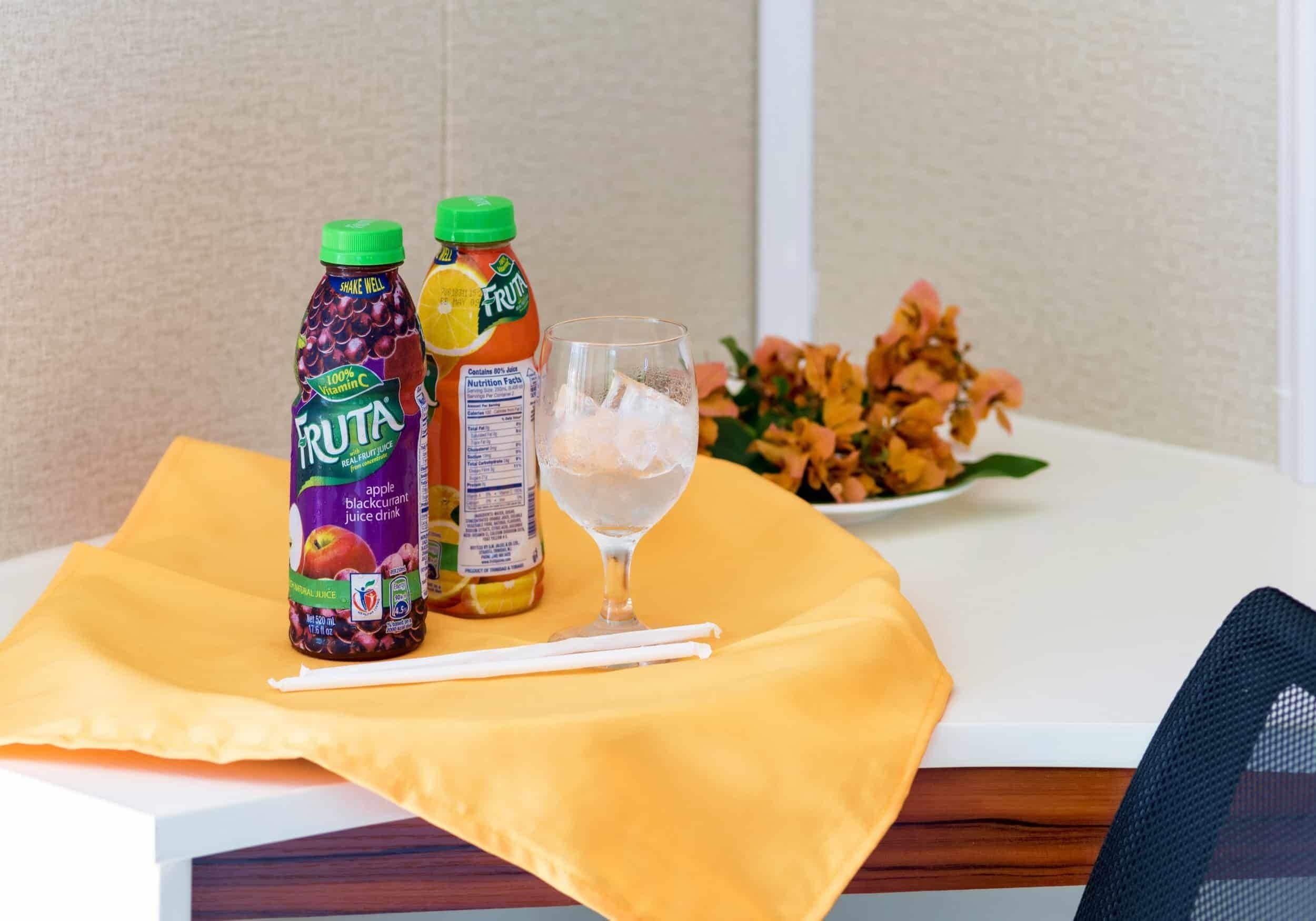 A table with two bottles of fruit juice, a glass of water, and a yellow cloth.