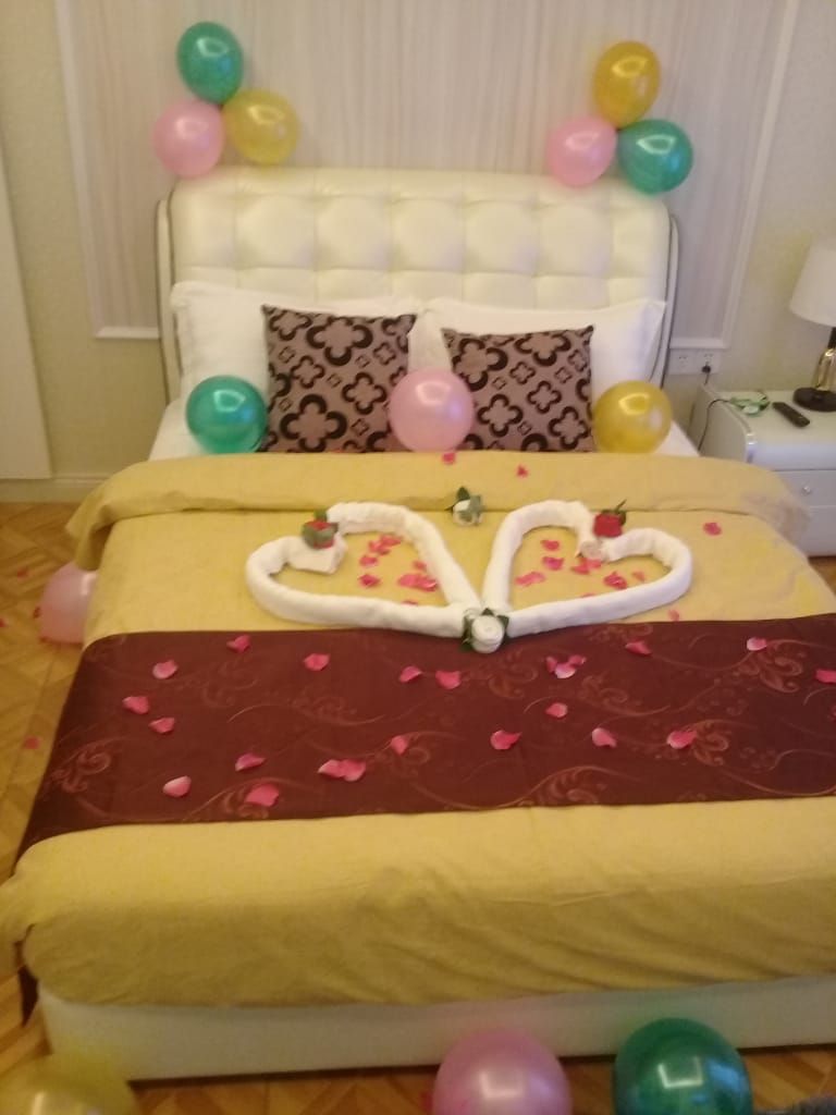 Una cama con una toalla dispuesta en forma de corazón, almohadas y globos.