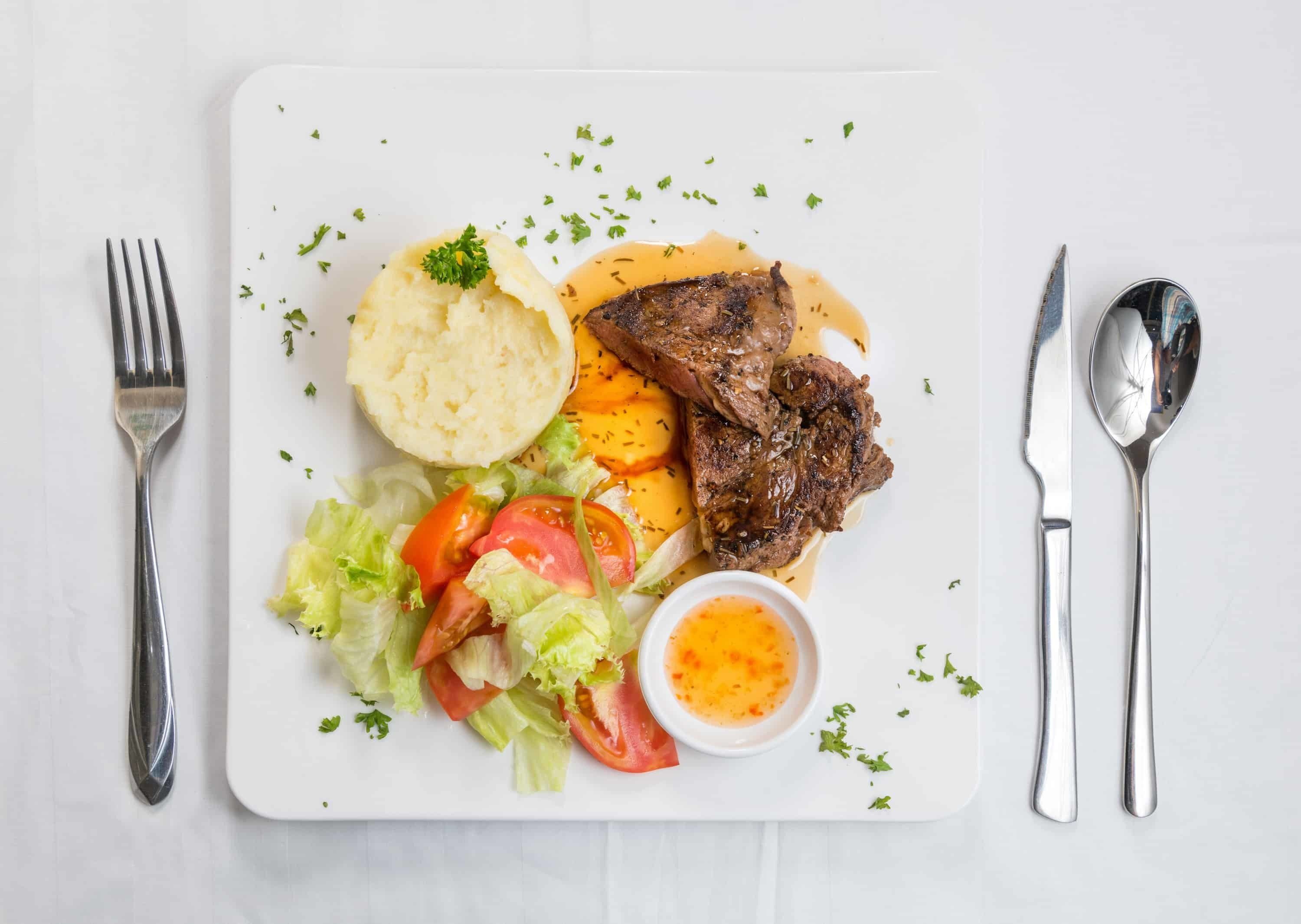 A plate with steak, mashed potatoes, and a salad, accompanied by cutlery.