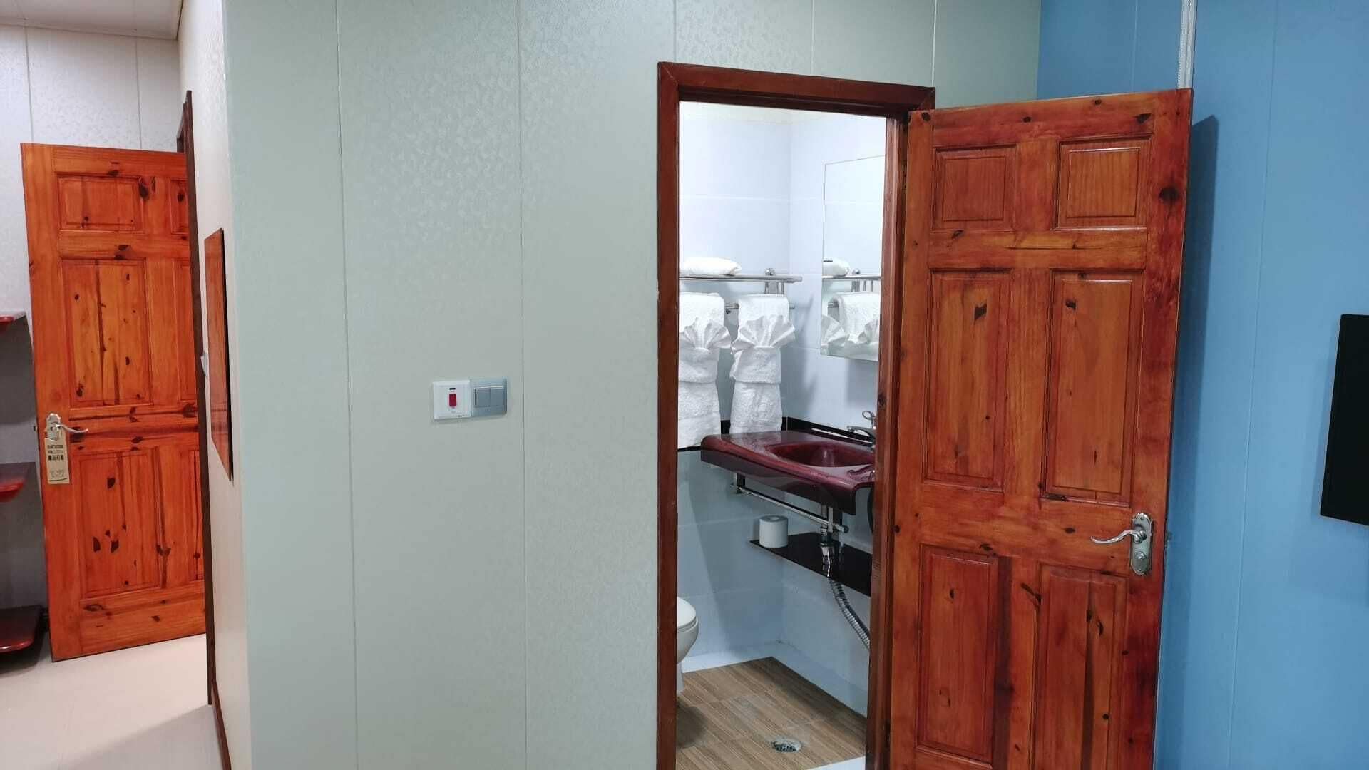 A bathroom with a wooden door, a white toilet, and a sink with a mirror.