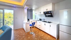 A modern kitchen with white cabinetry, a built-in microwave, and a refrigerator. There is a blue bar stool and a window with a view of greenery.