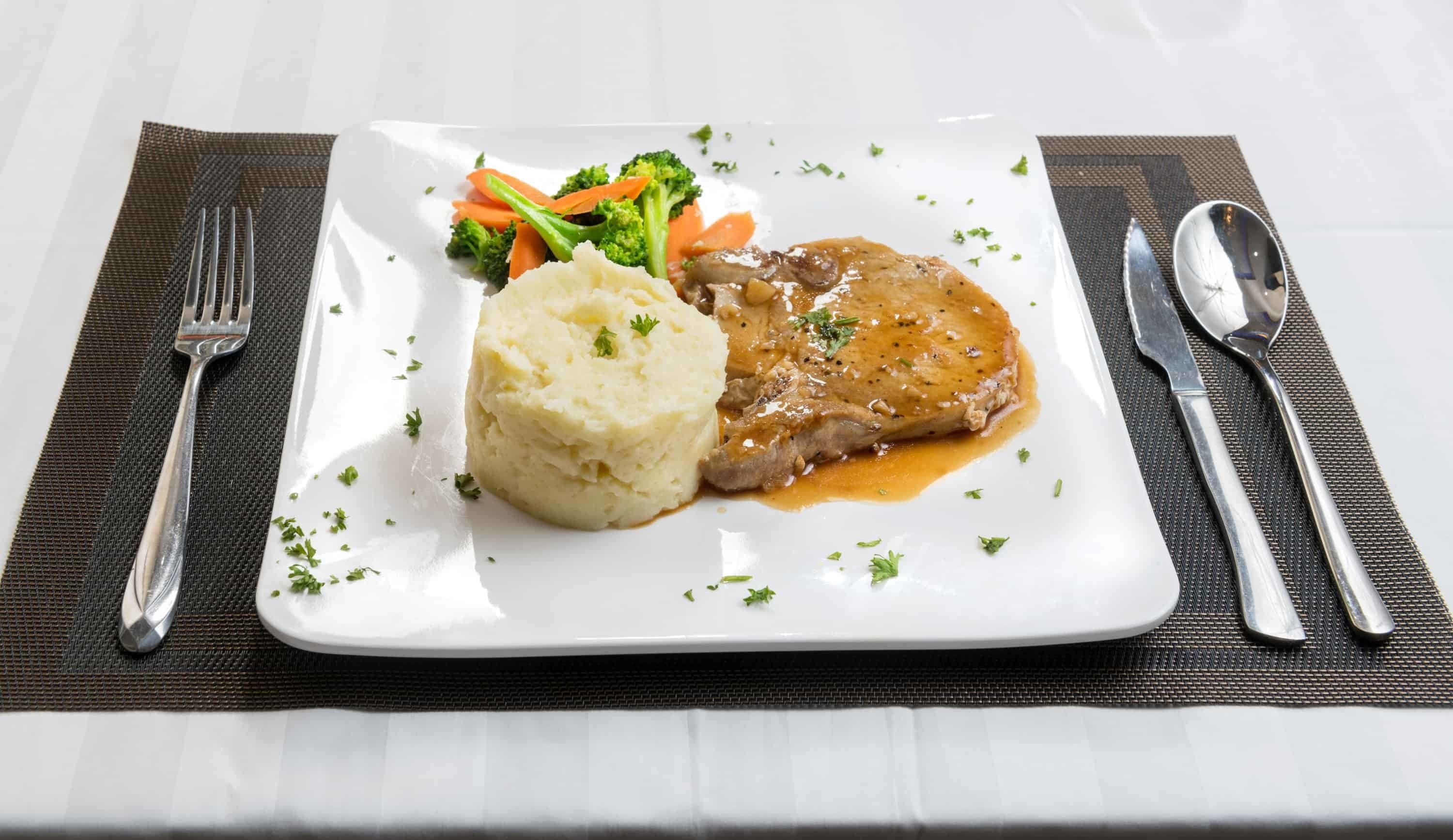 Un plato de puré de papas, un guiso de carne y verduras al vapor sobre un plato blanco y un camino de mesa negro.