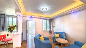 A modern room with a wooden floor, a red chair, two blue sofas with yellow cushions, a small wooden table, and a window with curtains. - Riverside Hotel (Portsmouth)