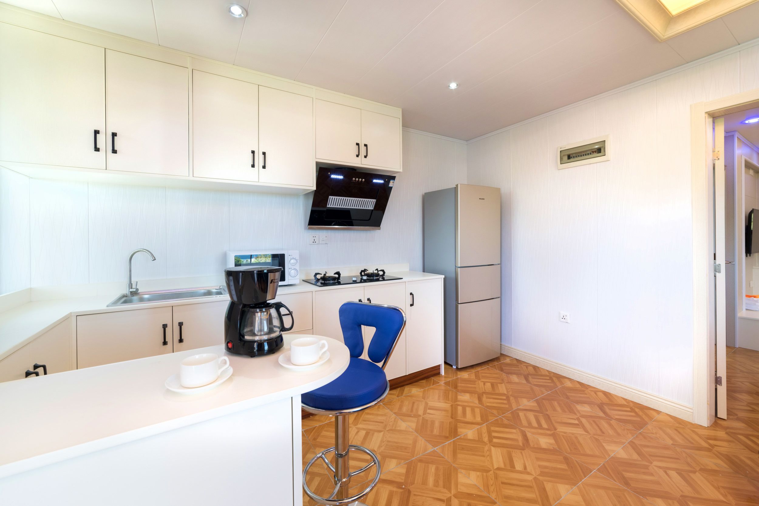 A modern kitchen with white cabinets, a coffee maker, a kettle, and a blue chair.
