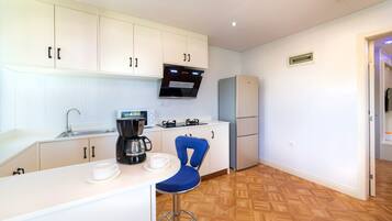 Una cocina moderna con armarios blancos, cafetera, hervidor y una silla azul.