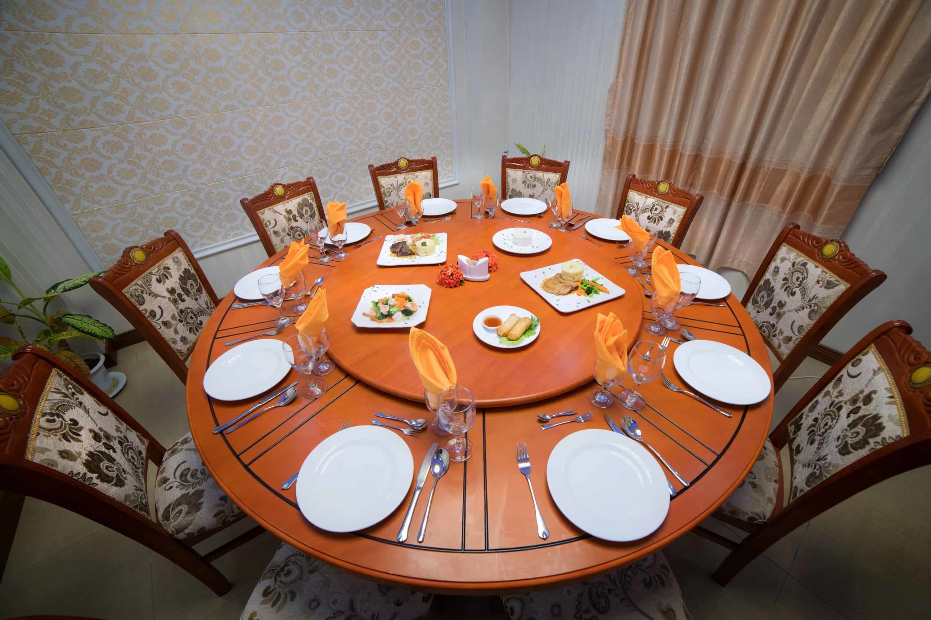 A round dining table with eight chairs, each with a floral-patterned cushion. The table is set with white plates, silverware, and glassware.